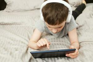 child boy lying on bed with pc tablet with wireless headphones photo