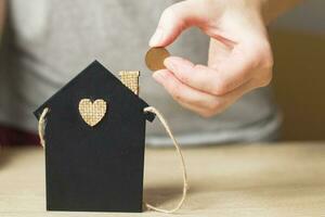 mano de mujer sosteniendo una moneda cerca de la casita de juguete. concepto de ahorro para el hogar foto