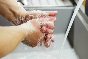 A man washes his hands with soap under the tap under running water close-up. Health, and hygiene concept. photo