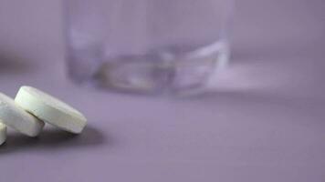 Píldoras de tabletas solubles efervescentes y vaso de agua sobre fondo púrpura video