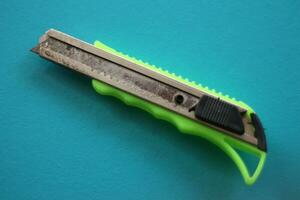 Close up view of green cardboard cutter isolated on blue background Isolated box cutter. photo
