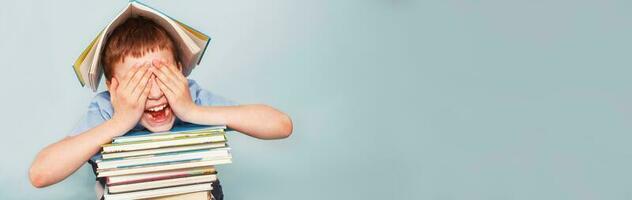 schoolboy sitting with pile of school books and covers his face with hands isolated on a blue background photo