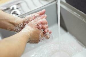 A man washes his hands with soap under the tap under running water close-up. Health, and hygiene concept. photo