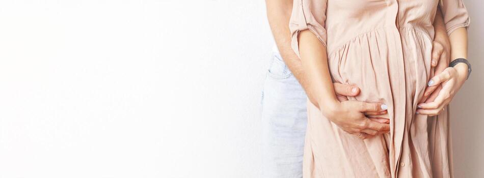 Young pregnant woman and husband hugging her belly close. banner photo