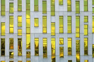 KATOWICE, POLAND, 2021 - Fragment of office building facade made of yellow toned glass and concrete constructions. Frontal view. Reflection of the sky and cityscape in the mirrored windows photo