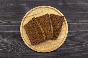 Pieces of rye flour black bread on a wooden serving plate and bl photo