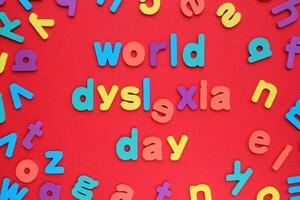 World dyslexia day words and random wooden colorful alphabet letters on red background. Learning difficulties, reading problem, dyslexia concept photo