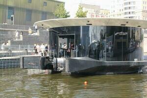 Pier dock of aquabus boat on Moskva River. Electrical ship at Moscow public transport. Ecological technology. Green energy in city route. Daily passenger ferry service. Moscow, Russia - June 22, 2023. photo