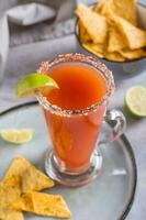 Michelagua mocktail with tomato juice and lime juice in a glass and nachos in a bowl vertical view photo