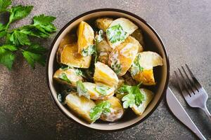 Close up of potato salad in a peel with parsley and mayonnaise in a bowl on the table top view photo