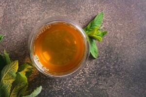 Close up of fresh mint tea in a cup and leaves on the table top view photo