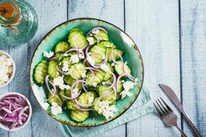 Fresh cucumber, ricotta and red onion salad on a plate on the table top view photo