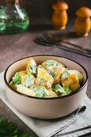 Potato salad in a peel with parsley and mayonnaise in a bowl on the table vertical view photo