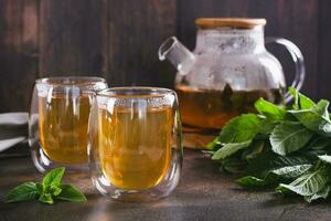 Fresh mint tea in cups and teapot and leaves on the table photo