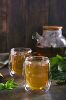 Fresco menta té en tazas y tetera y hojas en el mesa vertical ver foto