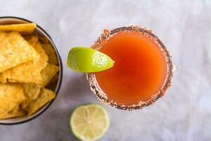 Close up of michelada cocktail with tomato juice, beer and lime in a glass and nachos top view photo