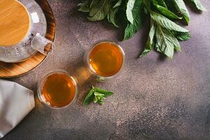 Fresh mint tea in cups and teapot and leaves on the table top view photo