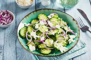 Diet salad of cucumbers, red onions and ricotta on a plate on the table photo