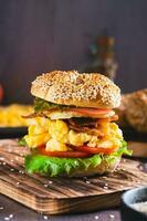 Homemade bagel with scramble egg, bacon, cheese, tomato and lettuce on a board vertical view photo