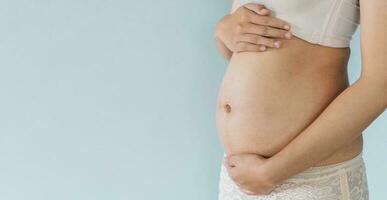 embarazada mujer sostiene manos en barriga y pastel color antecedentes. el embarazo, maternidad, preparación y expectativa concepto. de cerca, Copiar espacio. joven mujer esperando para bebé nacimiento. foto