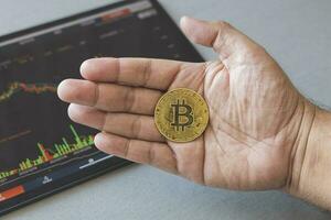 Close-up hand of man holding crypto coin on chart in tablet background. Blockchain technology finance future. Male hold bitcoin. concept about business, finance, trade, economy, banking, investment. photo