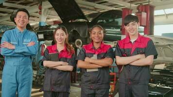 retrato de multirracial profesional mecánico equipo brazos cruzado y Mira a cámara, trabajo a coche Servicio cochera, contento mantenimiento trabajos, cheque y reparar ocupación en automotor industria negocio. video