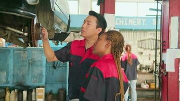 professionnel automobile superviseurs inspecter et discuter voiture suspension réparation travail avec femelle africain américain mécanicien ouvrier à un service garage, et réparer spécialiste métiers dans le auto industrie. video