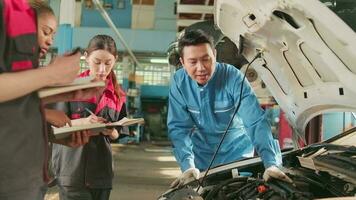 asiatisk manlig professionell bil- ingenjör handledare beskriver bil motor underhåll och reparera arbete med mekaniker arbetstagare staber team i fixera service garage, specialist yrken i bil industri. video