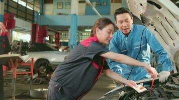 Asian male professional automotive supervisor advises and inspects a mechanic worker woman about liquid engine oil at car garage, service maintenance, and fix specialist occupations auto industry. video