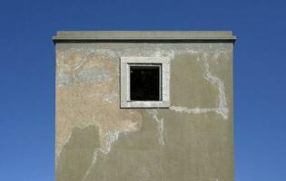 Symmetrical view of an abandoned building with a single window in the middle against a blue sky photo