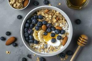 Bowl of greek yogurt with oatmeal granola, banana, blueberry, nuts, chia seeds and honey on gray table. Top view, generate ai photo