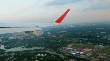 Visualizza di il ala di il aereo nel il oblò su il città e il aeroporto con pittoresco nuvole video