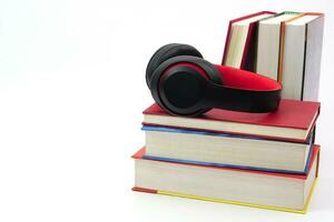 Focus of headphones are on stack of books and blur the many books lying in the background. Modern education and relaxation concept. photo