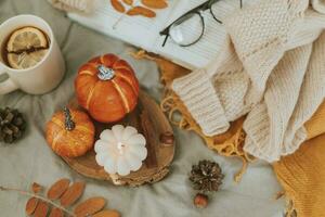 Burning candle, pumpkin decor and mug of lemon tea. Open book with eyeglasses and cozy sweater on bed. Autumn cozy home and hygge concept. Top view photo