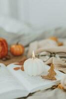 Burning candle shape of pumpkin. Open book, halloween decoration, cozy sweater and eyeglasses. Cozy autumn concept photo