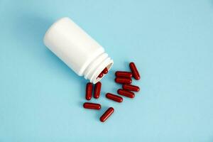 medical capsules of red color are poured out of an overturned bottle on a blue background photo