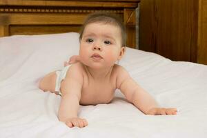 charming cute baby girl lies on her tummy on a light background and carefully looks around photo