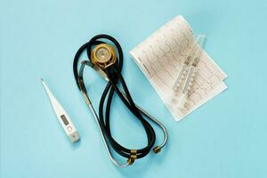 thermometer, phonendoscope, cardiogram, syringes on a blue background modern medicine. photo