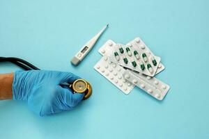 the hand of a medic holds a stethoscope, next to a thermometer and pills photo