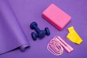 yoga brick, dumbbells, jump rope, fitness band on purple gym mat photo