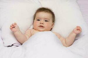 cute baby girl lies in bed and carefully looks at something photo