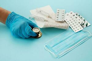 doctor's hand holding stethoscope next to cardiogram, syringes, mask and pills photo