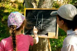 madre y hija en el jardín jugando tic-tac-toe en un pizarra tablero. foto