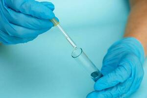 gloved hand dripping liquid from a pipette into a test tube photo