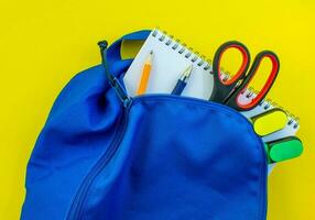 School backpack, pencil, pen, markers, scissors and notepad on a yellow background. photo