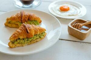 Croissant sandwich with egg,avocado on white dish and honey, coffee. breakfast and healthy food concept. photo