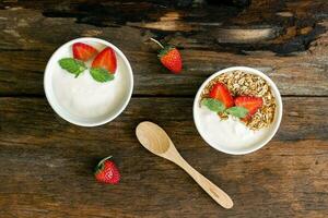 Strawberry yogurt in a wooden bowl with granola, mint and fresh strawberry on wooden background. Health food concept photo