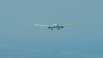 Plane approaching to land, front view. Airliner in the blue sky over the sea. Tourism and travel concept video