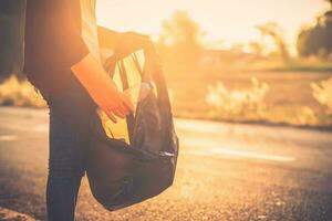 mujer son coleccionar basura en el la carretera con el fondo de el puesta de sol. limpiar arriba a reducir global calentamiento foto