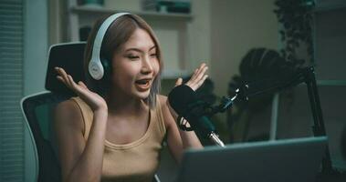 antal fot av ung asiatisk kvinna influencer bär hörlurar talande in i en mikrofon medan inspelning en radio visa i en levande rum Hem studio. innehåll skapare och influencer marknadsföring begrepp. video